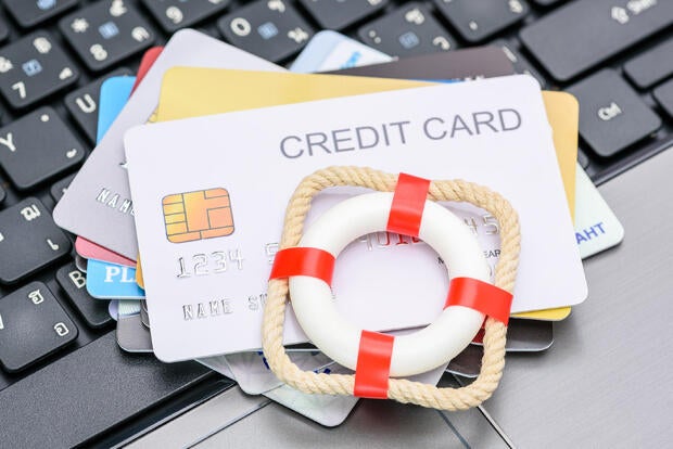 Household and credit card debt, personal loan, payment overdue, financial problems : Red lifebuoy or lifebelt atop a stack of credit cards on a laptop, depicting problems in repaying credit card debt.