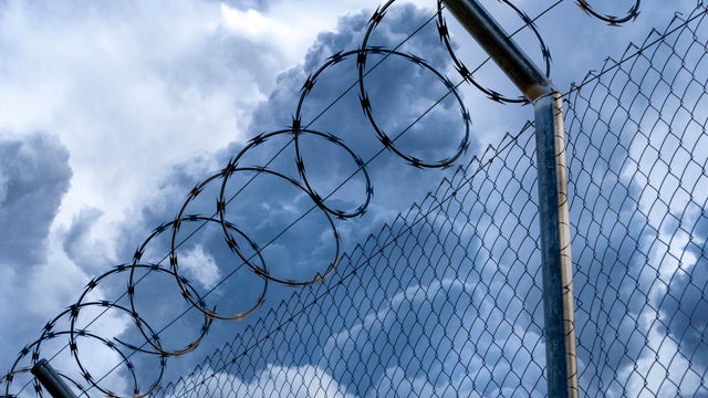 Close-up of metal fence with barbed wire over a stormy blue sky. 