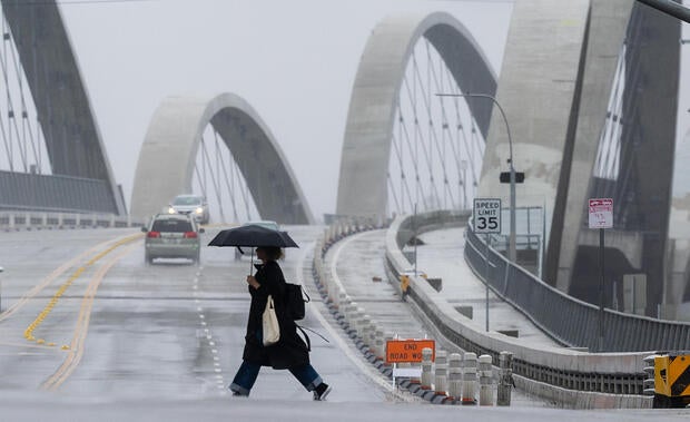 A pedestrian crosses the street in the rain with a view of the The Sixth Street Viaduct 