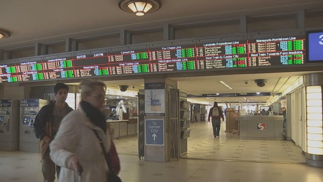 People walk under the boards showing train times at 30th Street Station in Philadelphia 