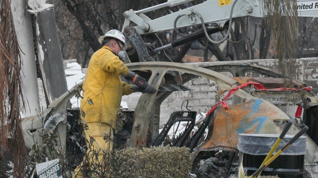 Workers handling the charred remains of an electric vehicle after California wildfires 