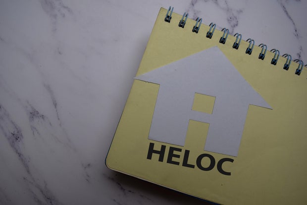 HELOC write on sticky note and house made from paper isolated on Office Desk.