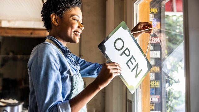 Female small business owner placing open sign in business window 