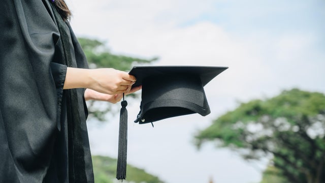 Student wearing graduation gown and holding a graduation cap. 