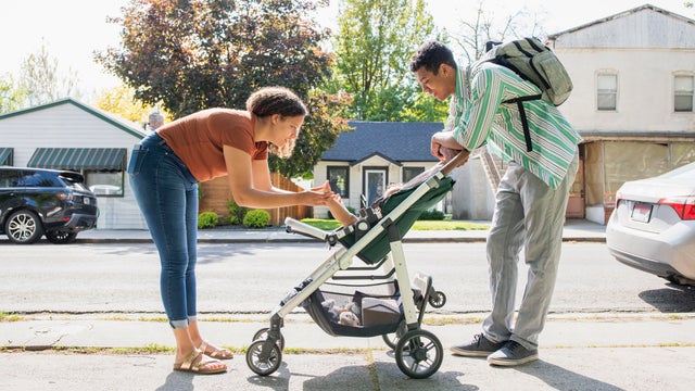 Mother and father playing with baby daughter in stroller on city street 