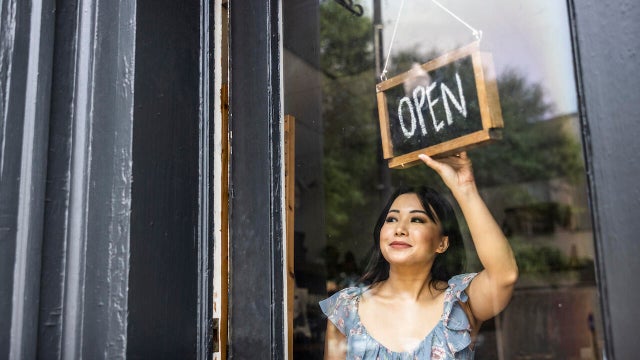 Female small business owner turning open sign in her store 