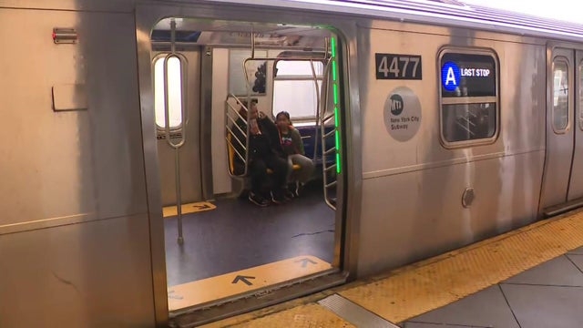 Two riders sit on an A train stopped at a station. 