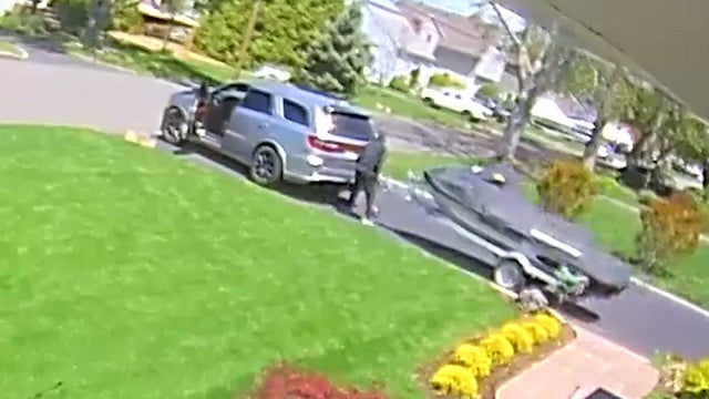 An individual in a hoodie attaches a watercraft on a trailer to a minivan. 