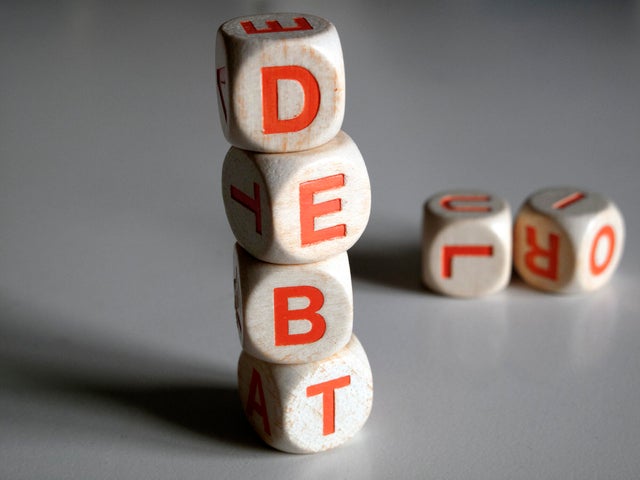 White and orange scrabble dice spelling the word "DEBT" 