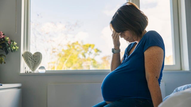 Mature pregnant woman sitting on her bed - negative emotion 