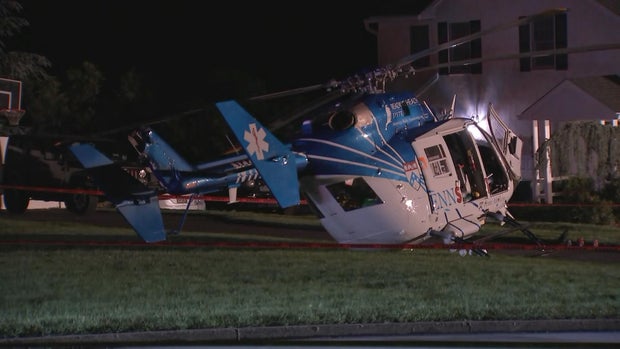 A small medical helicopter with some minor damage is seen in the yard of a suburban house in 