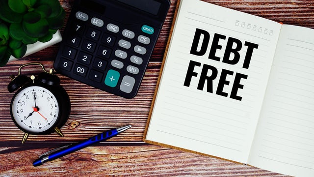 Debt Free text written on paper torn with calculaton and alarm clock top view on wooden background 