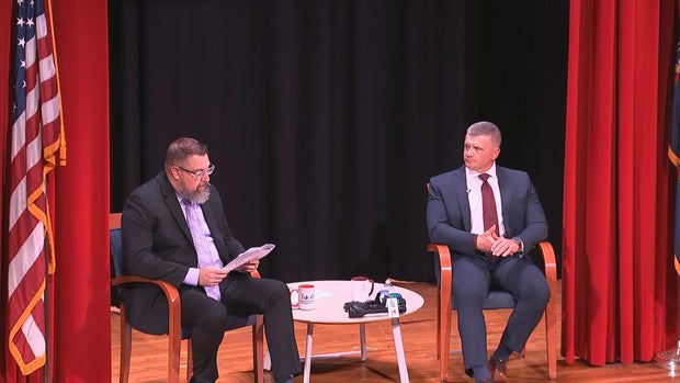 Two men sit on a stage during an event 