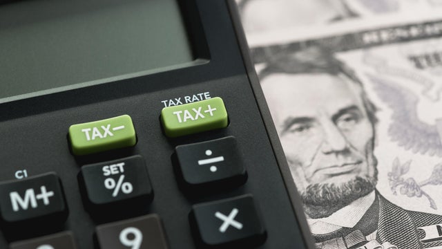 Closed up shot of TAX minus / plus buttons with text TAX RATE on calculator with background of US Dollar banknotes, United States government tax calculation 