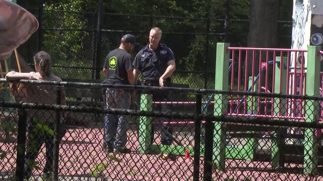 An NYPD officer and a NYC Parks employee stand on a playground near a jungle gym. 
