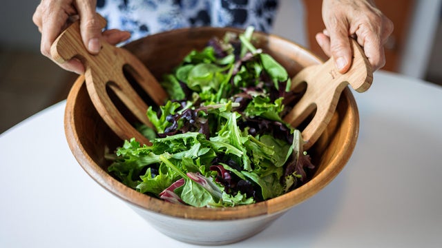 Female hands mixing various vegetable in wooden salad bowl. 