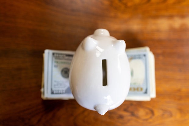 white piggy bank on top of stack of u.s. paper bills 