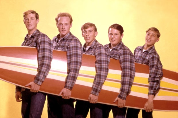 The Beach Boys - from left, Brian Wilson, Mike Love, Dennis Wilson, Carl Wilson and David Marks - pose for a portrait with a surfboard in August 1962 in Los Angeles, California.