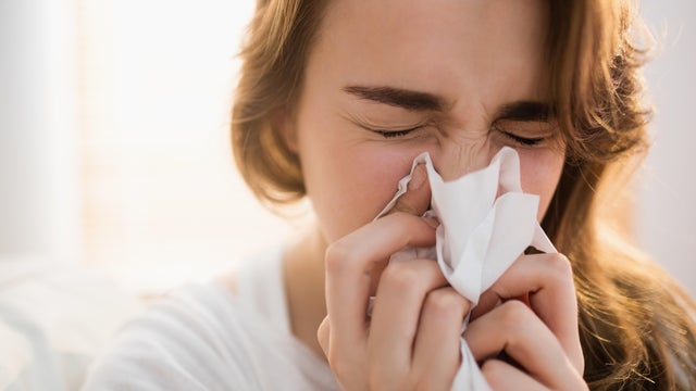 Woman blowing her nose on couch 