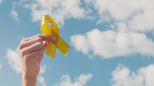 Hands holding yellow gold ribbon over blue sky, Sarcoma Awareness, Bone cancer, childhood cancer awareness, September yellow, World Suicide Prevention Day concept 