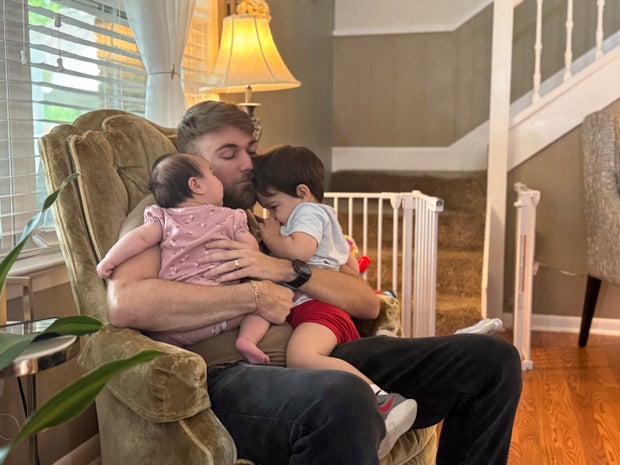 U.S. Marine Corps veteran Adrian Clouatre holds his 3-month-old daughter Lyn and his nearly 2-year-old son Noah at their home in Baton Rouge, Louisiana, June 17, 2025.