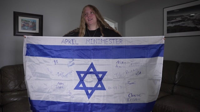 A New Jersey teenager holds an Israeli flag with multiple signatures and the words "April minimester" on it. 