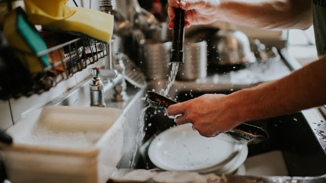 A man washes dishes in a commercial kitchen environment 