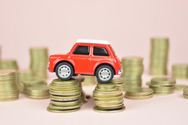 Red car toy on stacks of coins. Pink background. 