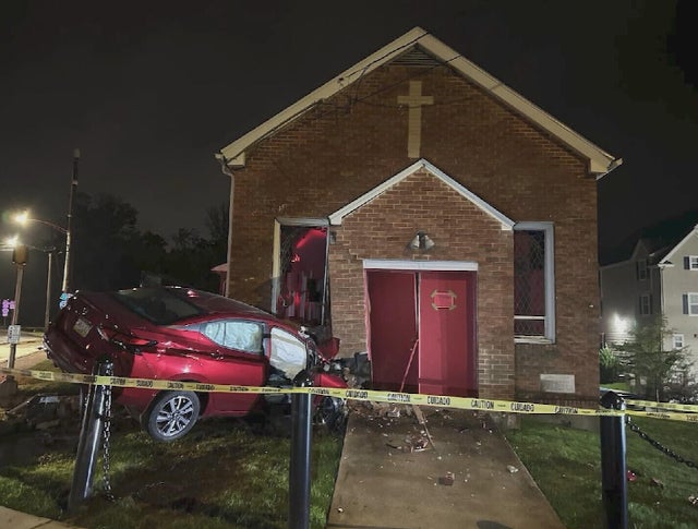 A car has crashed into a small church, caution tape surrounds the scene 