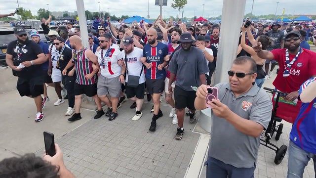 A large crowd of fans linking arms walk outside MetLife Stadium 