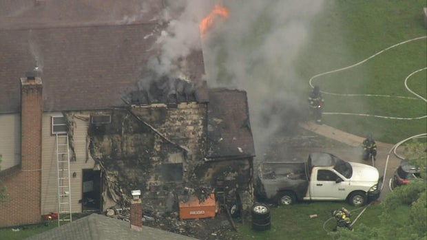 Overhead photo of a house fire, the back of the home is damaged and appears charred, flames and smoke are seen on the home 