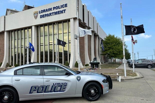 Candles sit on a memorial and flags fly at half-staff outside the police department in Lorain, Ohio, on July 24, 2025, a day after a deadly ambush. 