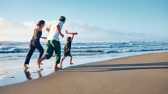Parents running behind a boy running straight ahead with a model airplane held high in one hand. 