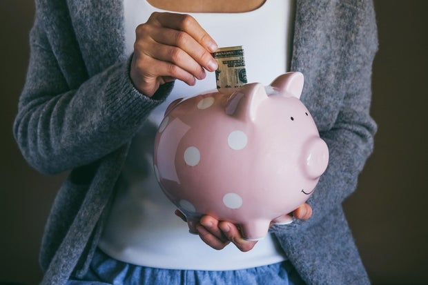 Woman putting bill in happy piggy bank. Female saving money for household payments, bank bills, calculating monthly family budgets, making investments strategy for retirement. 