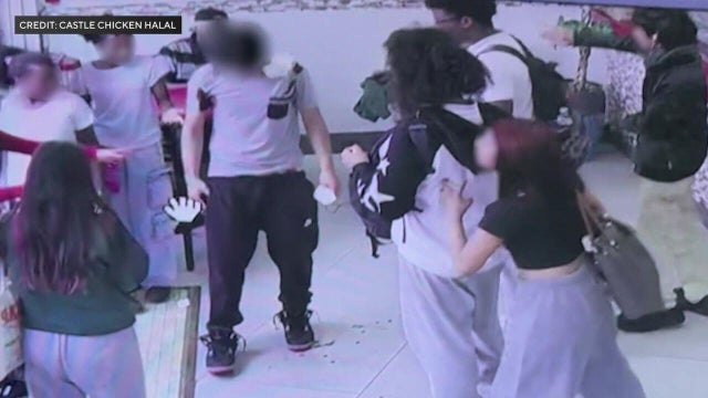 A teenager who is bleeding from multiple wounds stands in the middle of a restaurant surrounded by teen onlookers 
