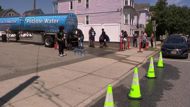 A potable water truck in a parking lot with people lining up to get water 
