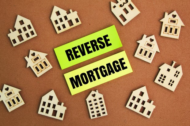 the shape of a wooden house and paper with the word reverse mortgage 