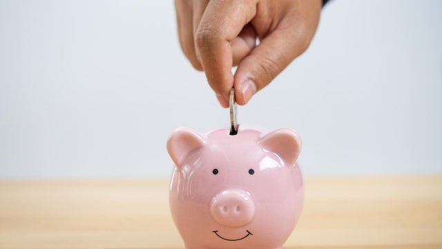 Businessperson's Hand Putting Coin In Piggybank 