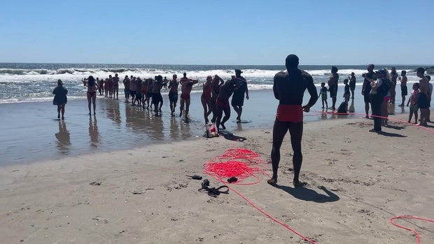 Lifeguards lined up along the shore pulling a rope 