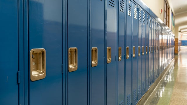 Photo of a blue metal lockers along a nondescript hallway in a typical US High School. No identifiable information included and nobody in the hall. 