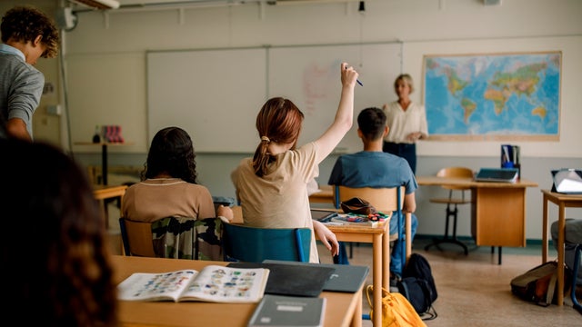 Teenage girl raising hand in high school classroom 