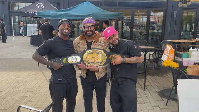 Three people pose for a photo with the wrestling-style belt they won at the Hoagie Throwdown 