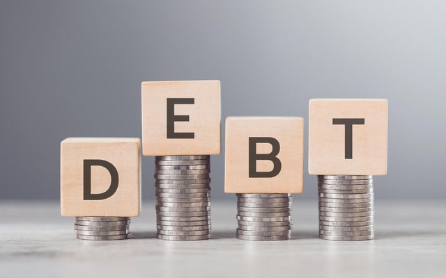Stack of coins neatly arranged on top of a wooden block labeled DEBT, symbolizing financial burdens and the weight of monetary obligations, set against a neutral background to emphasize the concept 