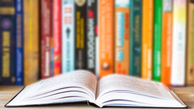 Close-up of opened book on bookshelf on blurred books background. Home library reading books concept 