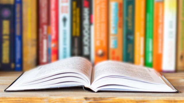 Close-up of opened book on bookshelf on blurred books background. Home library reading books concept 
