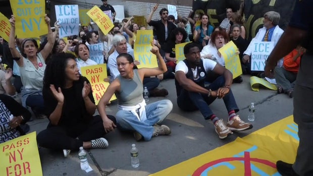 Jumaane Williams and other protesters with anti-ICE signs sit on the ground. 
