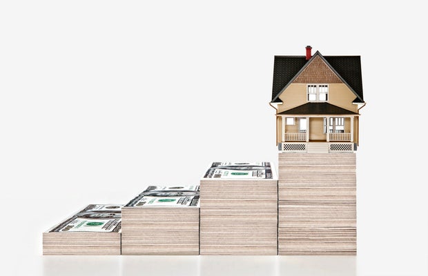 Four stacks of money with a house on the highest 
