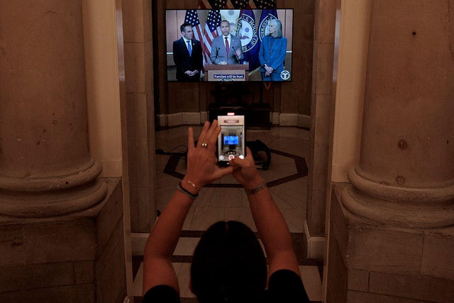 House Speaker Mike Johnson of Louisiana places a television in the doorway of his Capitol office in Washington, D.C., on Sept. 30, 2025, showing video of Democrats discussing a government shutdown.