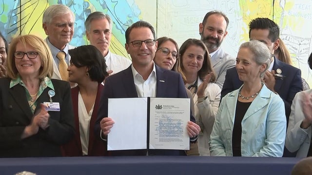 Surrounded by health care workers, Gov. Josh Shapiro holds up the executive order 