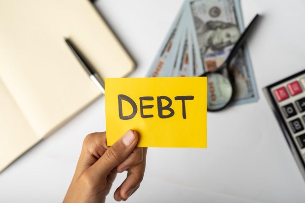 Hands Holding "DEBT" Label with Financial Tools and Money